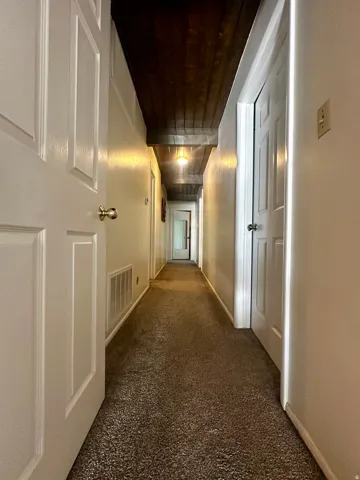 Elongated hallway featuring a dark wood-plank ceiling, recessed lighting, and light brown carpeting