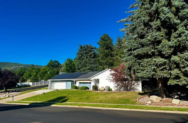 Ranch-style residence featuring a white exterior, attached two-car garage, and a black shingle roof with solar panels