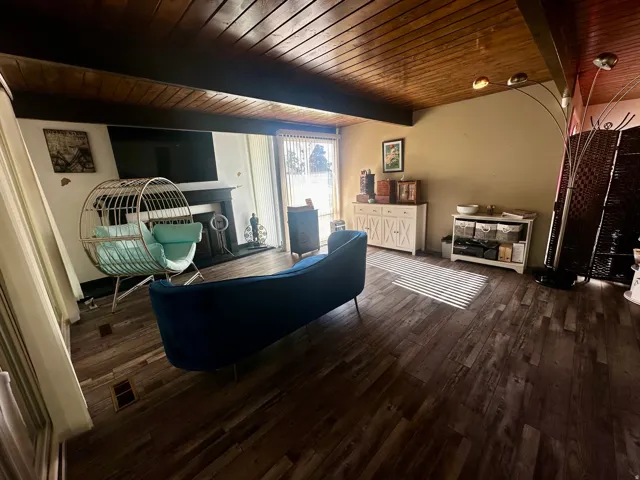 Living area featuring wood-finish flooring, a dark wood plank ceiling with exposed beams, a fireplace with a dark mantel, and sliding glass doors
