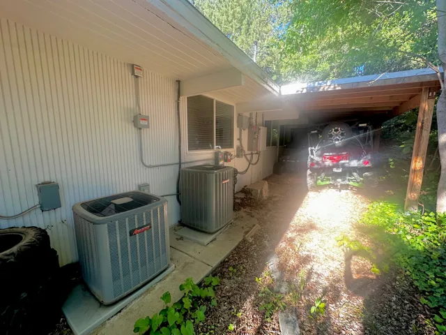 Exterior siding with horizontal paneling, two visible HVAC units, and a covered carport structure
