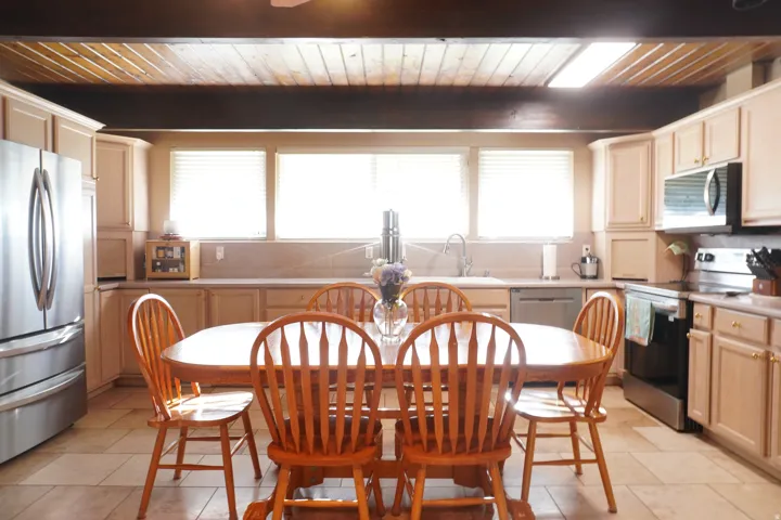 Kitchen featuring wood-finish ceiling, exposed beams, tile flooring, light-toned cabinetry, and stainless steel appliances