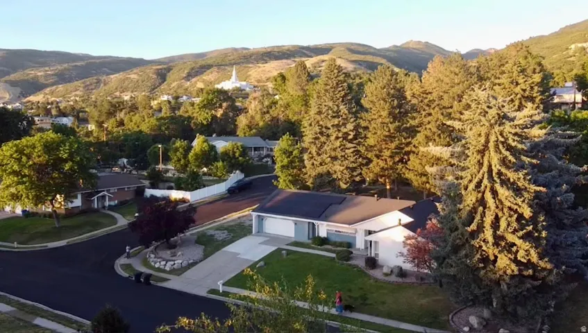 Ranch-style residence featuring a two-car garage, mature landscaping, and an asphalt driveway