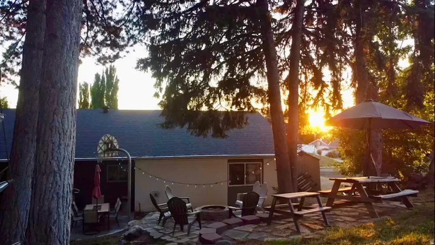 Backyard patio featuring a stone-paved fire pit area, string lighting, and mature trees providing natural shade