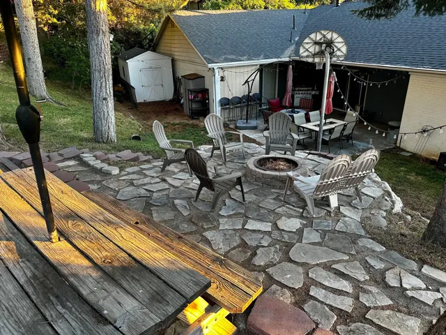 Expansive flagstone patio area featuring a built-in fire pit, an adjacent covered patio, and mature trees