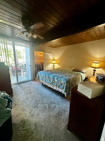 Bedroom featuring a wood-panel ceiling, light gray carpeting, and sliding glass doors leading to an exterior patio