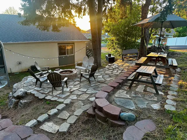 Stone patio featuring an integrated fire pit, string lighting, and multiple seating areas