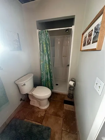 Bathroom featuring a stand-up shower with a white surround, a two-piece toilet, and large format floor tiles