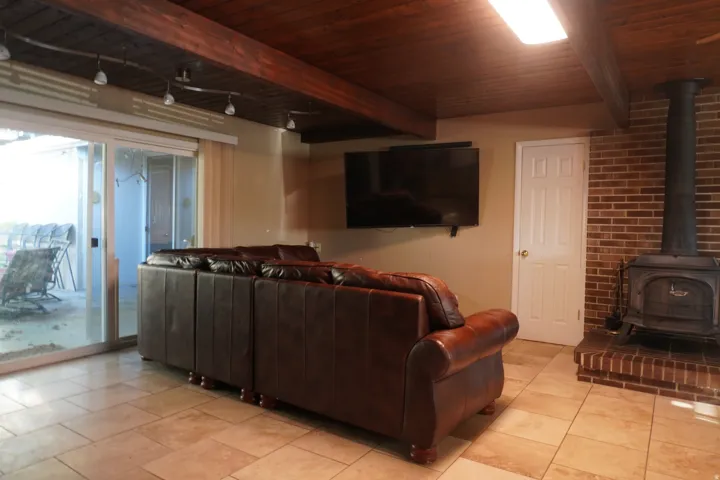 Living area featuring a brick accent wall with a wood-burning stove on a raised hearth, wood-paneled ceiling with exposed beams, and track lighting