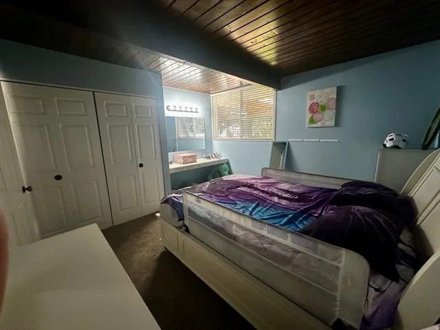 Bedroom featuring wood-paneled ceiling, bifold closet doors, and wood-finish flooring