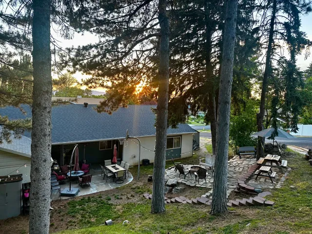 Expansive backyard featuring multiple patio areas, mature trees, a stone fire pit, and a separate storage structure