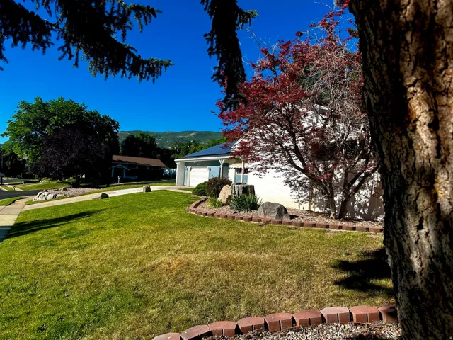 Expansive front yard with a green lawn, mature trees, and landscaping beds featuring decorative rocks and brick edging