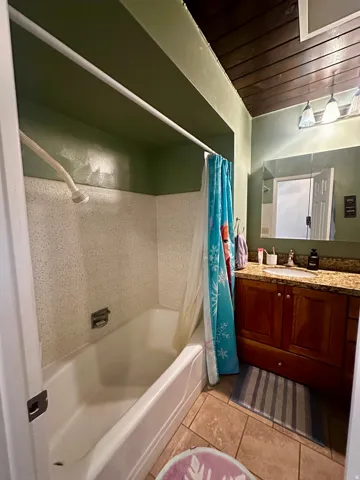 Bathroom featuring a built-in tub with tile surround, wood-paneled ceiling, recessed lighting, and a wood-finish vanity with a granite-look countertop