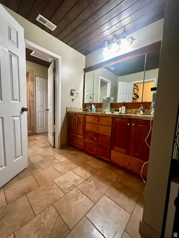 Bathroom featuring a dual vanity with a granite countertop, wood cabinetry, and a large wall-mounted mirror