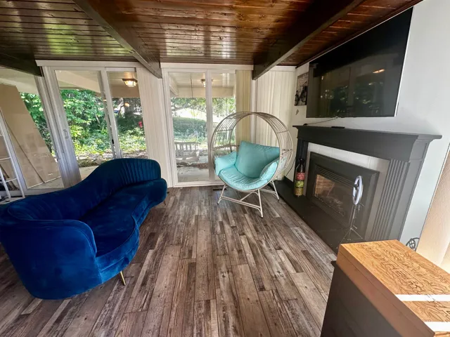 Room featuring wood-finish flooring, a prominent fireplace with a dark mantel, and a wood-paneled ceiling with exposed beams