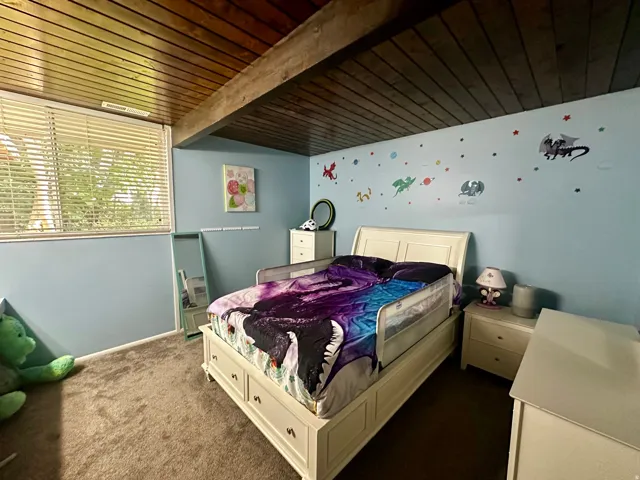 Bedroom featuring a wood-panel ceiling with exposed beam, light blue painted walls, and dark carpet flooring