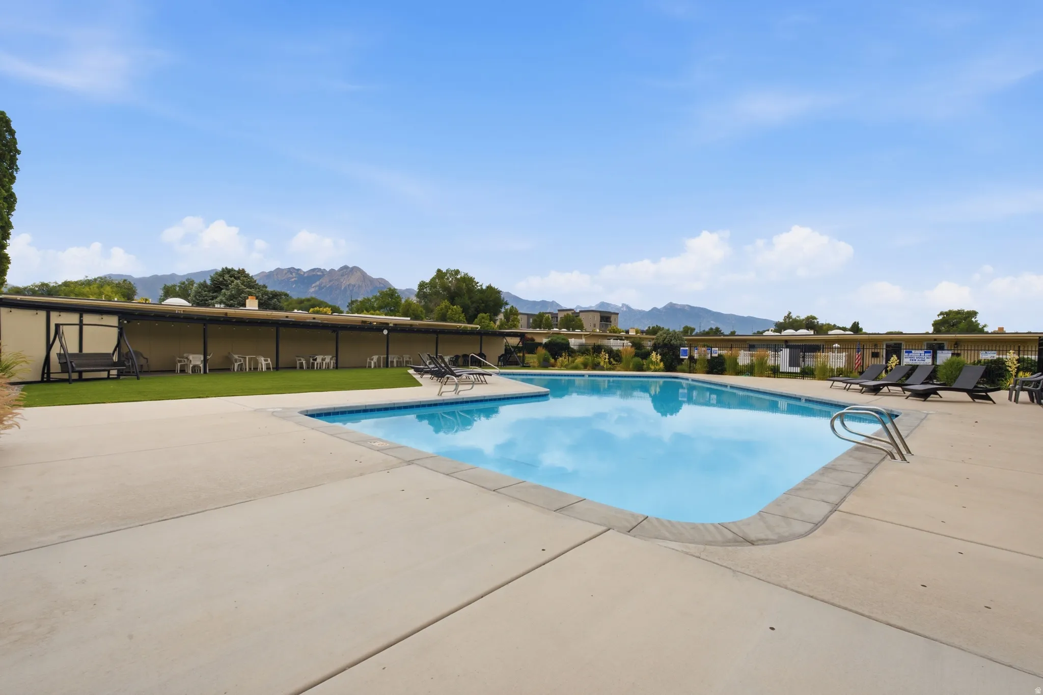 Outdoor swimming pool with concrete surround, bordered by a manicured turf area and mountain backdrop