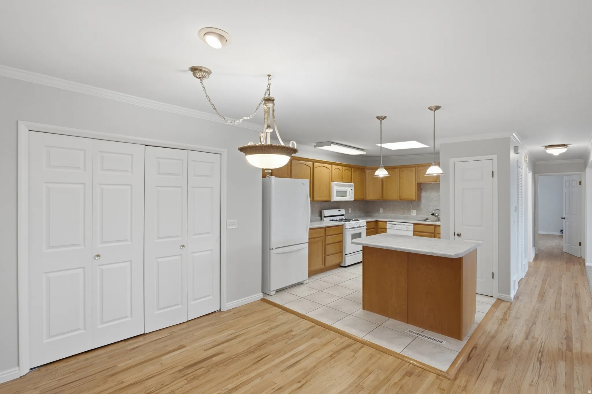 Open-concept kitchen featuring wood cabinetry, white appliances, and a central island with a light-colored countertop