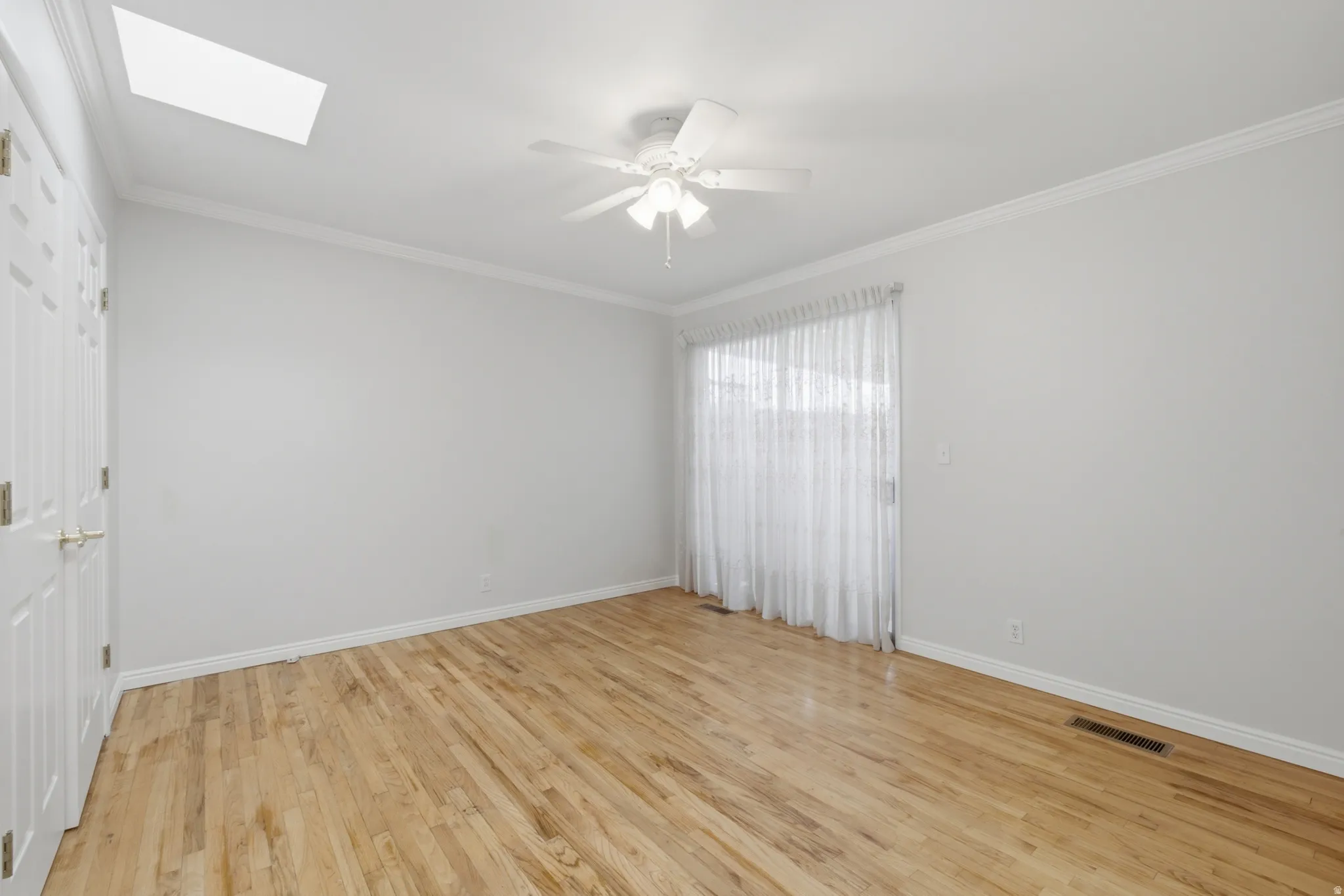 Light-filled room featuring wood-finish flooring, a ceiling fan, and a skylight