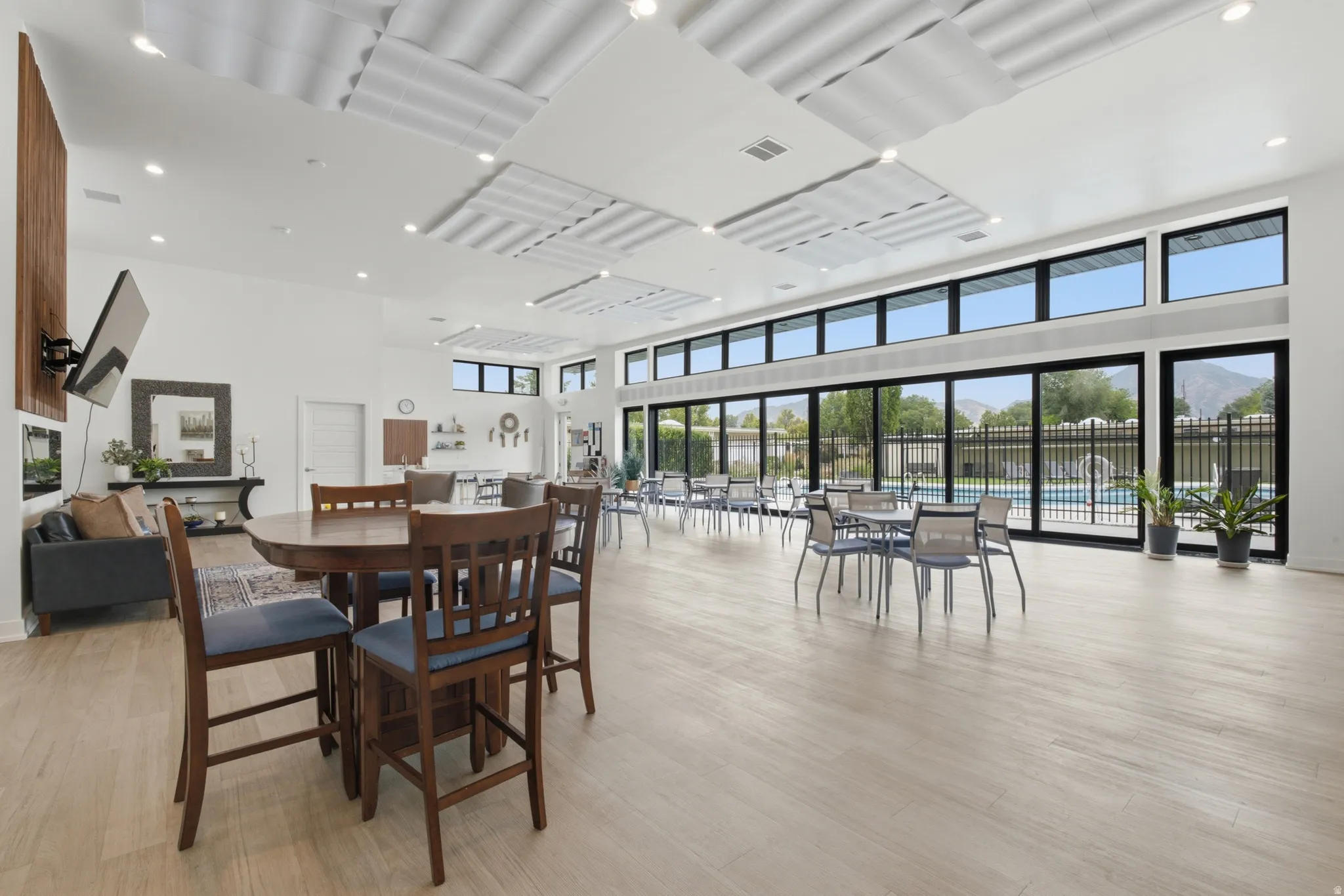 Spacious common area featuring light wood-finish flooring, a contemporary dropped ceiling design, and a full wall of floor-to-ceiling windows