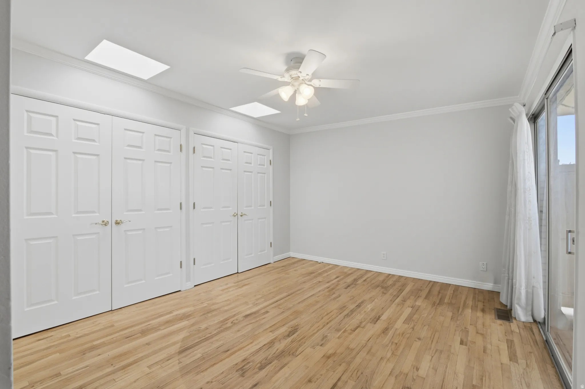 Bright interior space featuring wood-finish flooring, white paneled bifold doors, a ceiling fan, and a sliding glass door