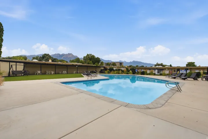 Outdoor swimming pool with concrete surround, bordered by a manicured turf area and mountain backdrop