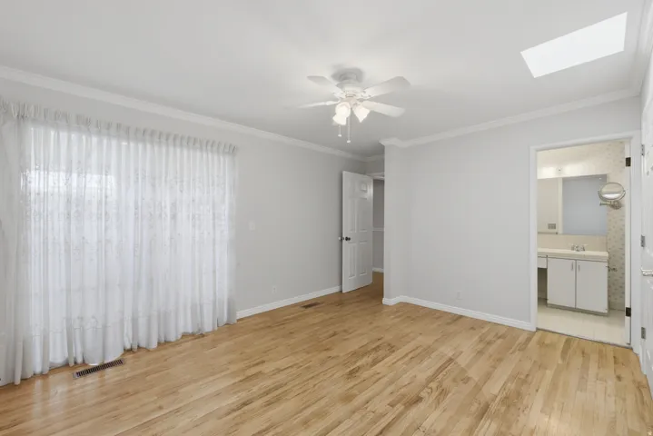 Room featuring wood-finish flooring, white crown molding, a ceiling fan with light fixture, and a skylight