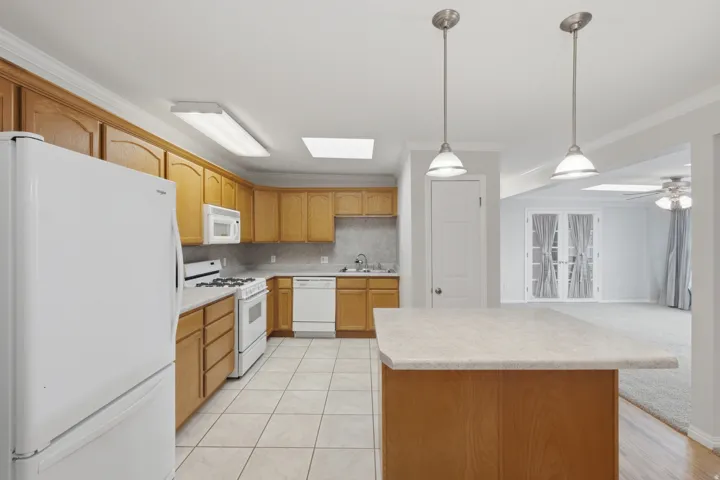 Kitchen featuring wood-finish cabinetry, tile flooring, white appliances, and a central island with a light-toned countertop
