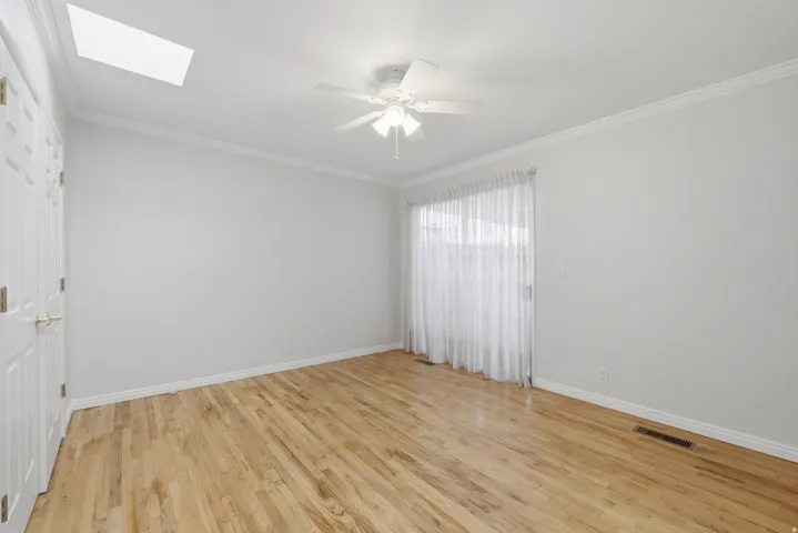 Light-filled room featuring wood-finish flooring, a ceiling fan, and a skylight