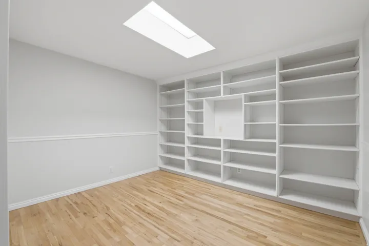 Room featuring extensive built-in white shelving, wood-finish flooring, a white ceiling, and a prominent skylight