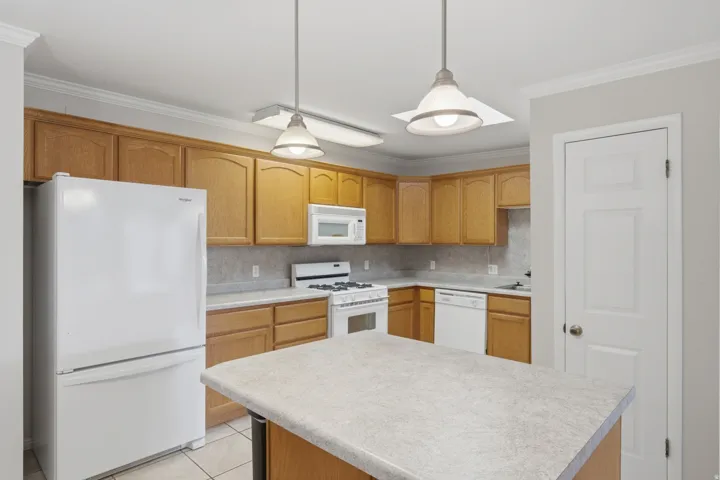 Kitchen featuring light wood-finish cabinetry, tile flooring, a central island with a light-toned countertop, and integrated white appliances including a refrigerator, range, and dishwasher