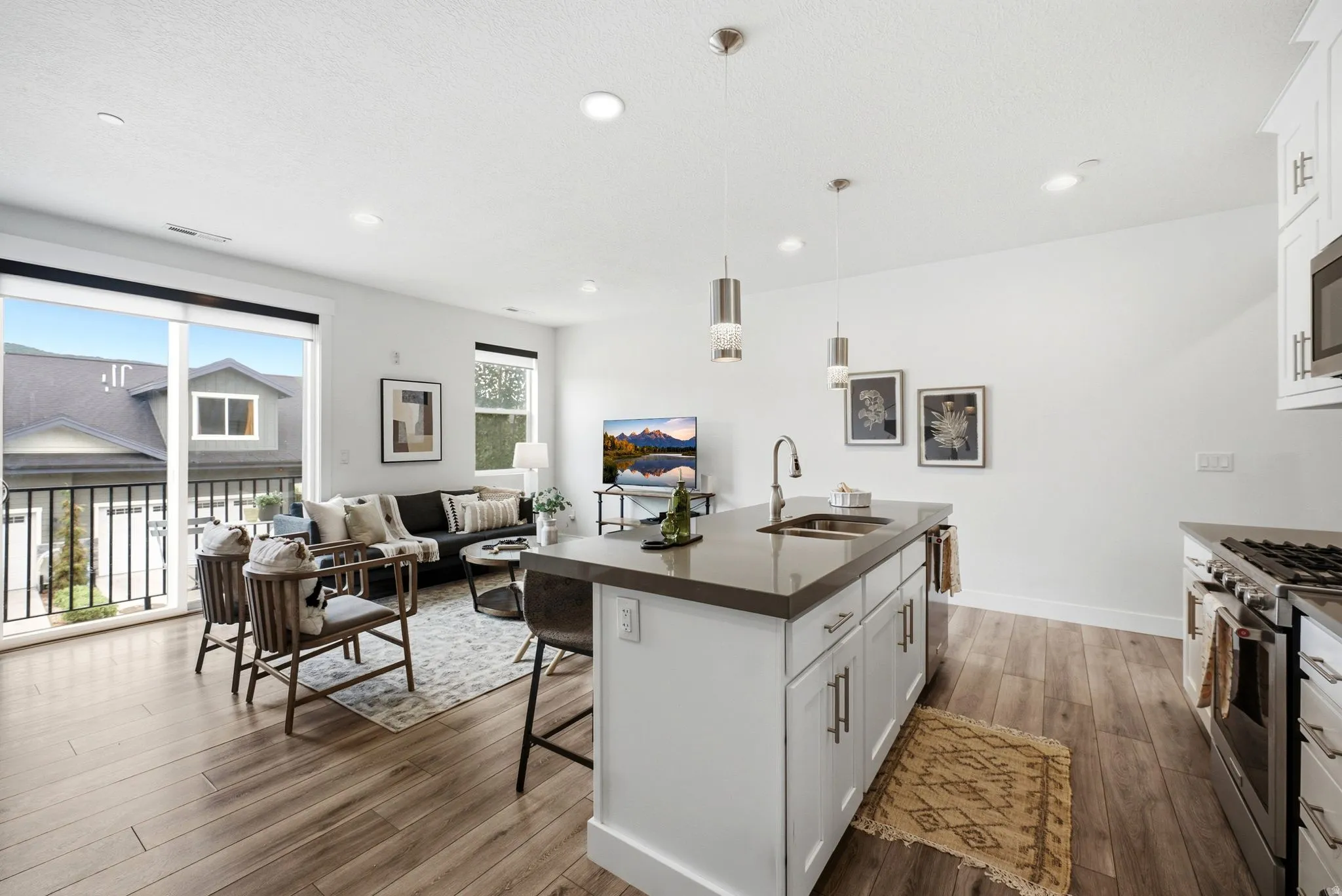 Open-concept living space featuring wood-finish flooring, recessed lighting, and a sliding glass door leading to a balcony with black railings