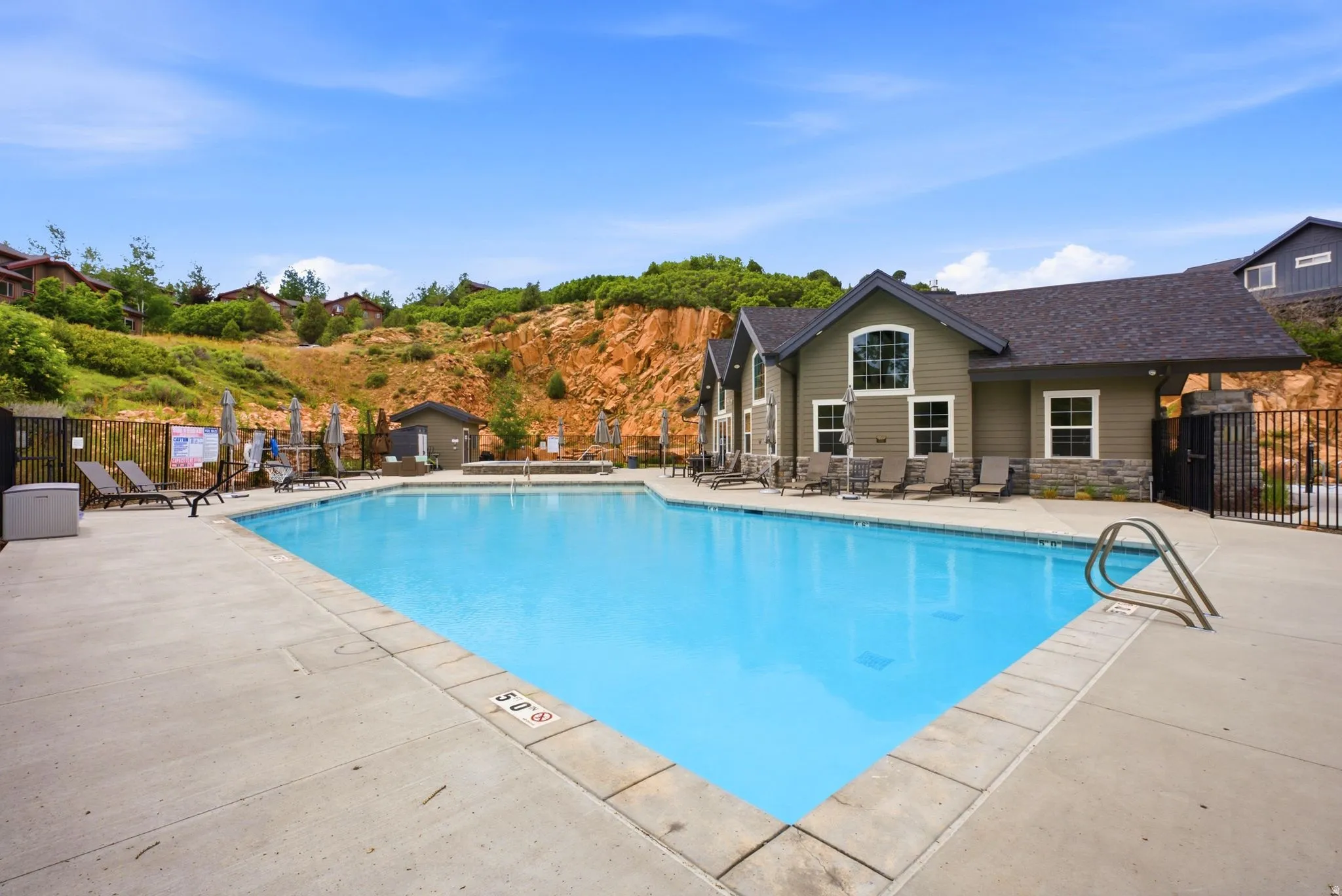 Rectangular swimming pool with integrated steps, surrounded by a concrete deck and a black metal fence