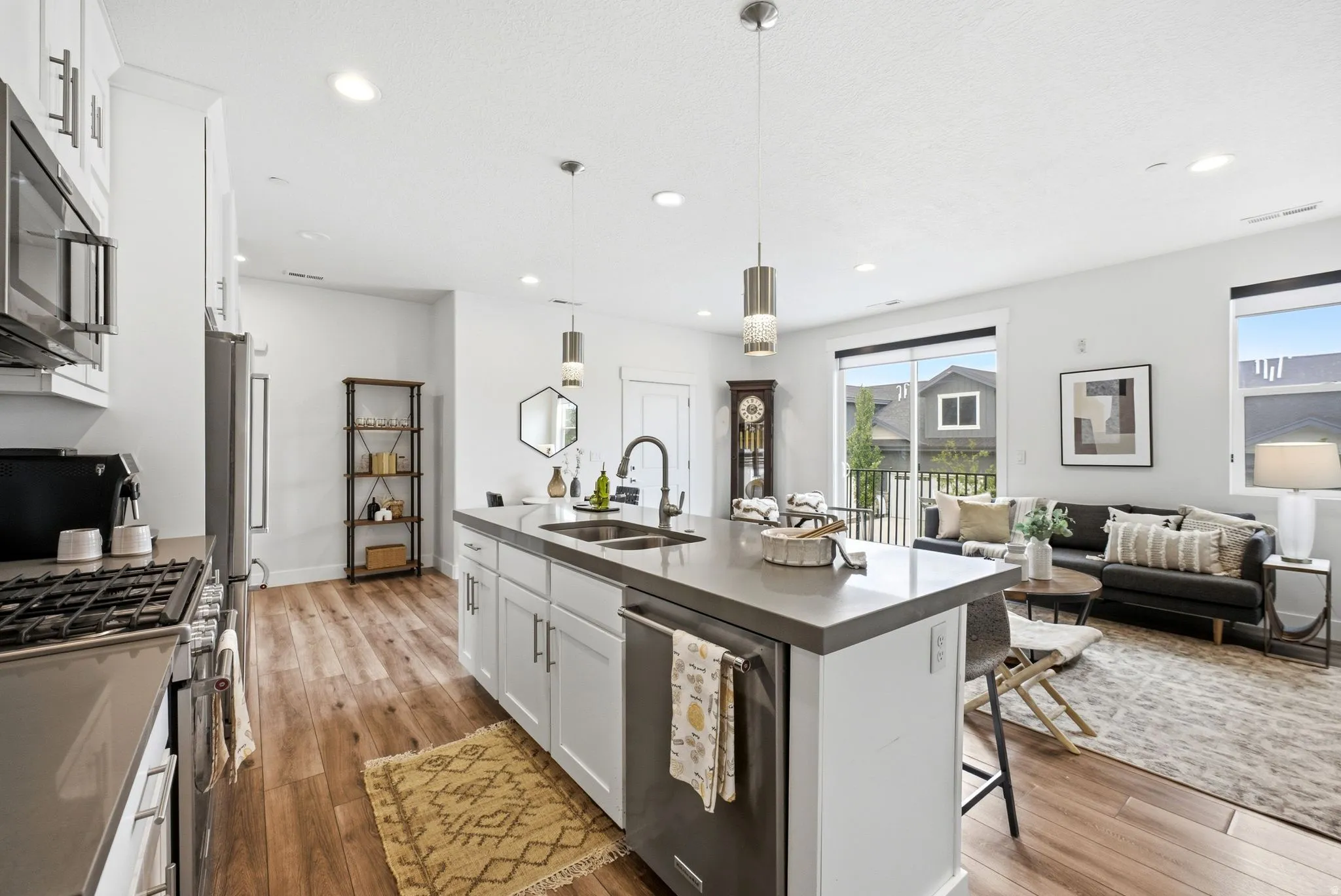 Open-concept kitchen featuring an island with a built-in sink and pendant lighting, stainless steel appliances, wood-finish flooring, white cabinetry, and recessed lighting