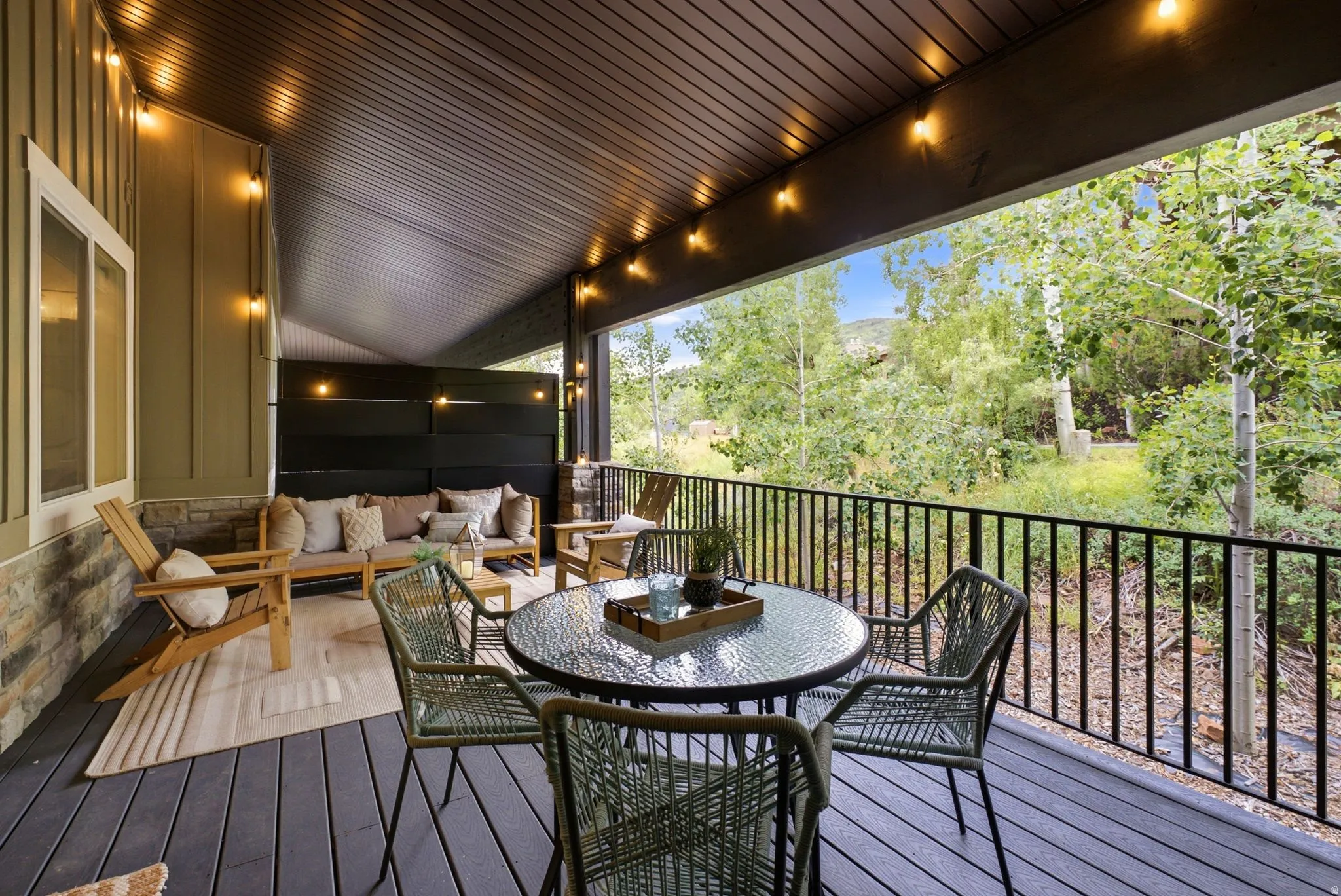 Expansive covered deck featuring composite wood-finish flooring, a stone accent wall, and a black metal railing
