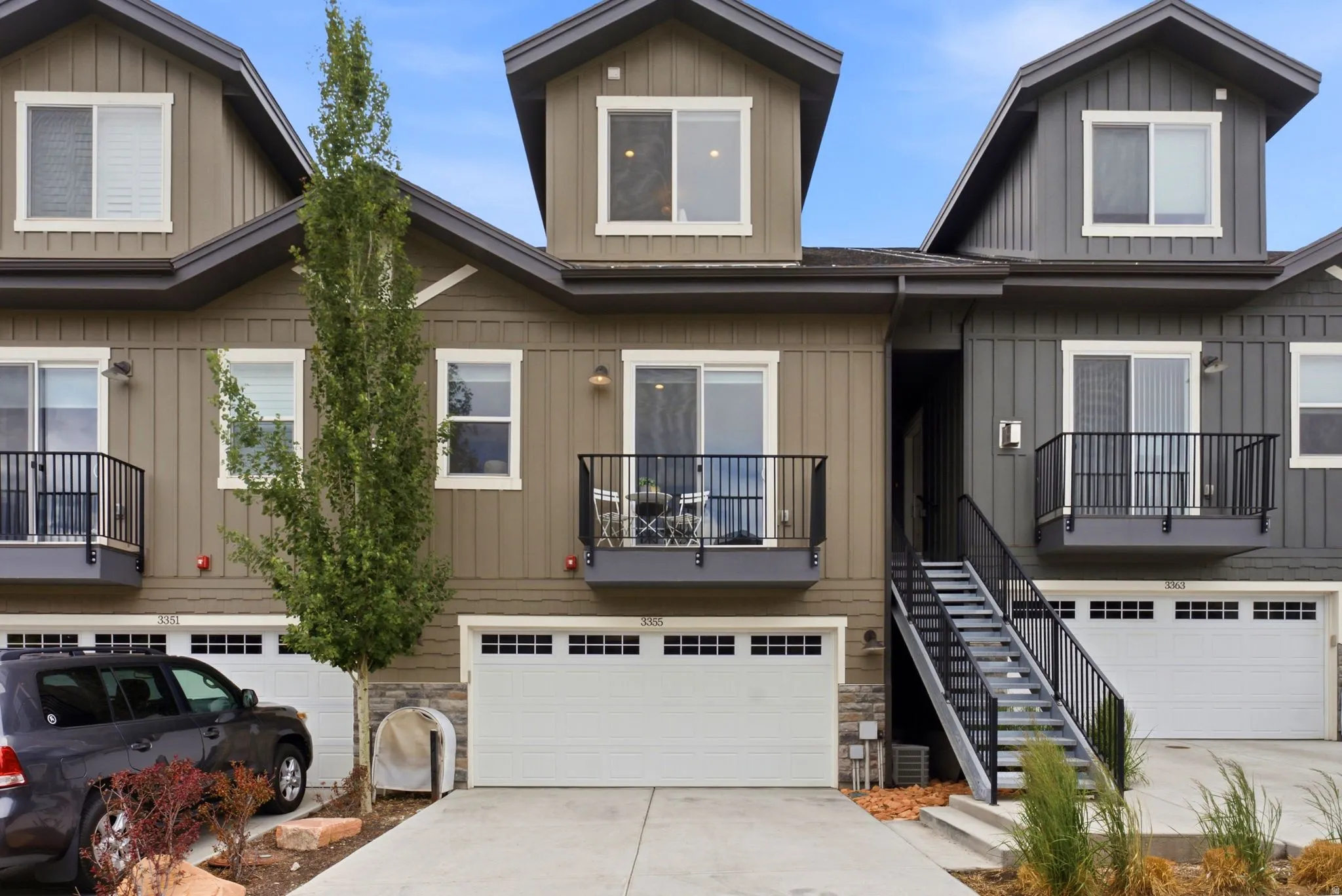 Contemporary townhome exterior featuring vertical siding, dormer windows, and a private balcony with black railings
