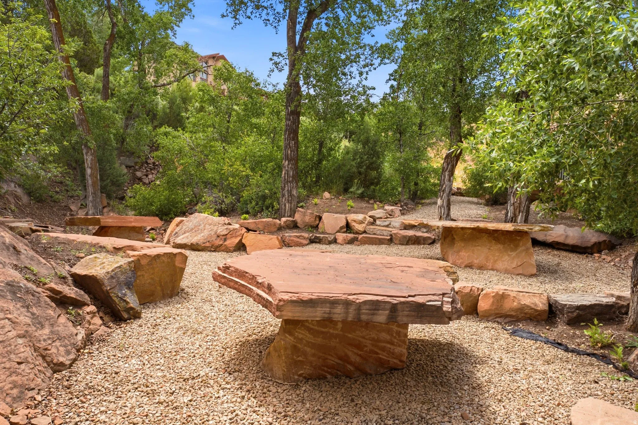 Landscaped outdoor area featuring a gravel ground cover, mature trees, and large natural stone elements