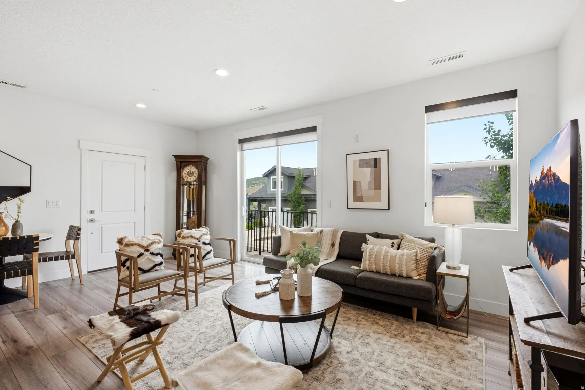 Open-concept living area featuring light wood-finish flooring, white walls, recessed lighting, and a sliding glass door to a balcony