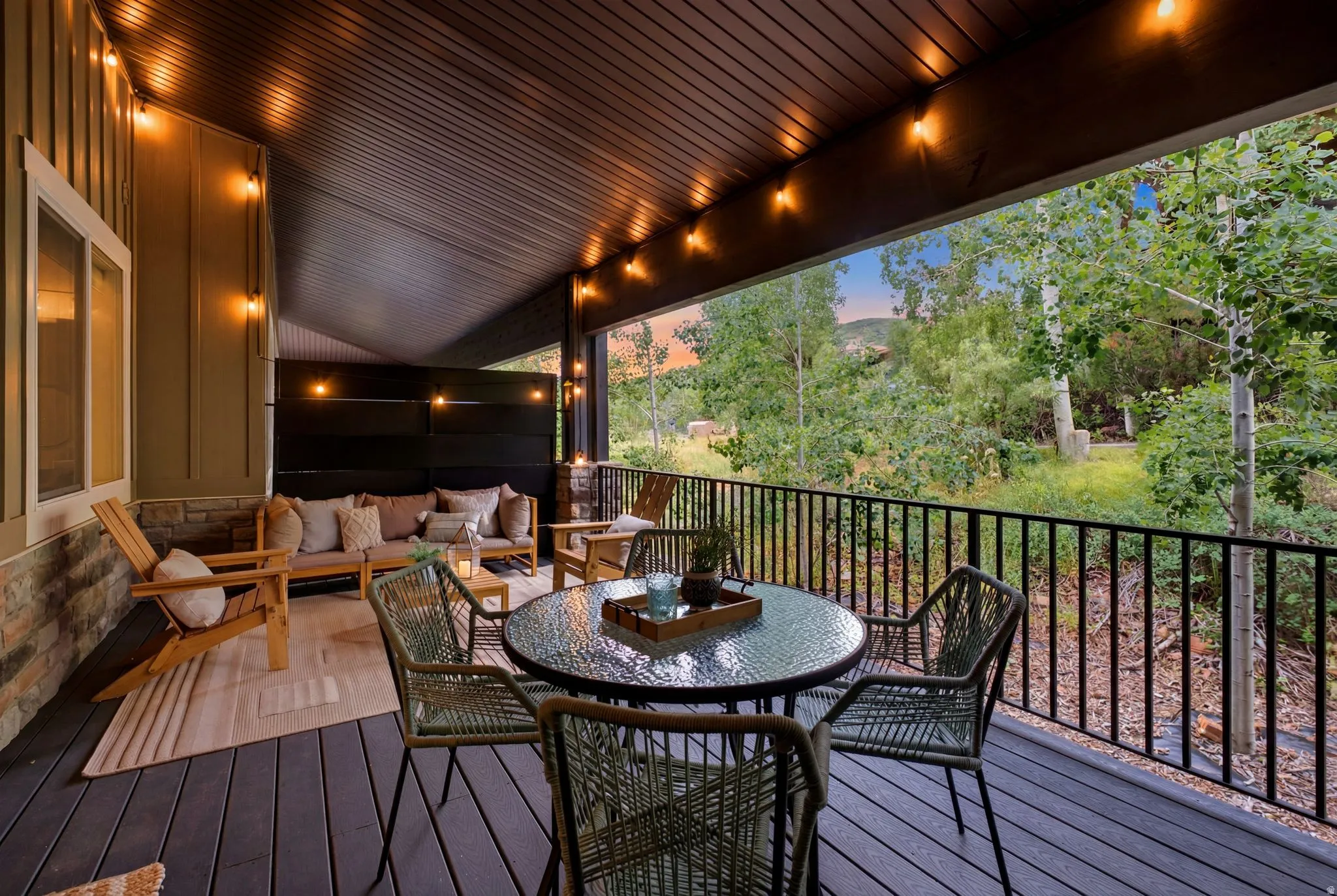 Expansive covered deck featuring dark wood-finish decking, stone accents, and string lighting