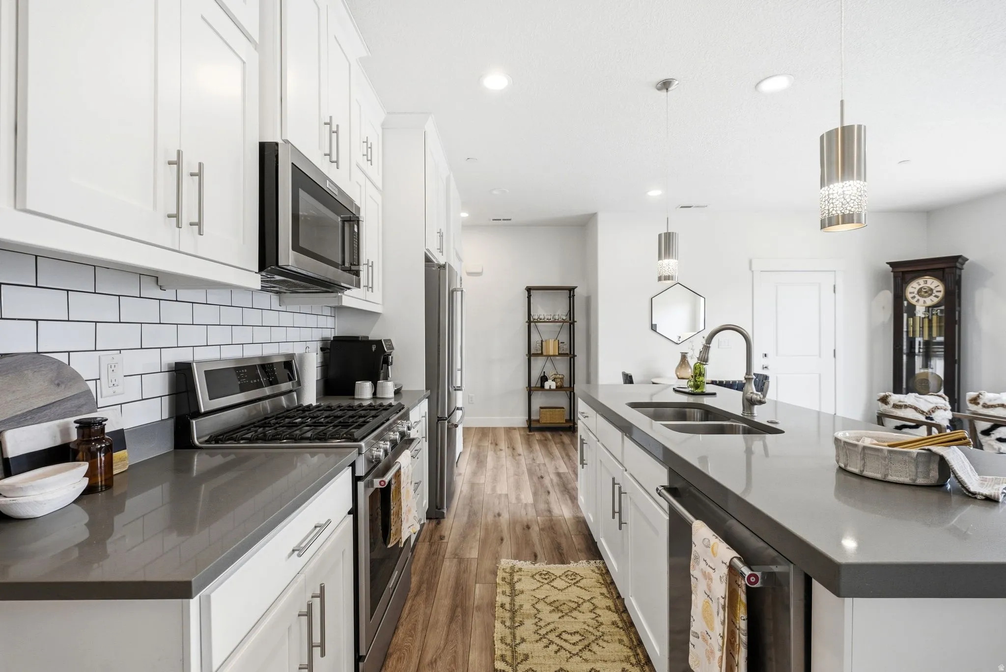 Kitchen featuring white shaker cabinetry, stainless steel appliances, grey countertops, white subway tile backsplash, and wood-finish flooring