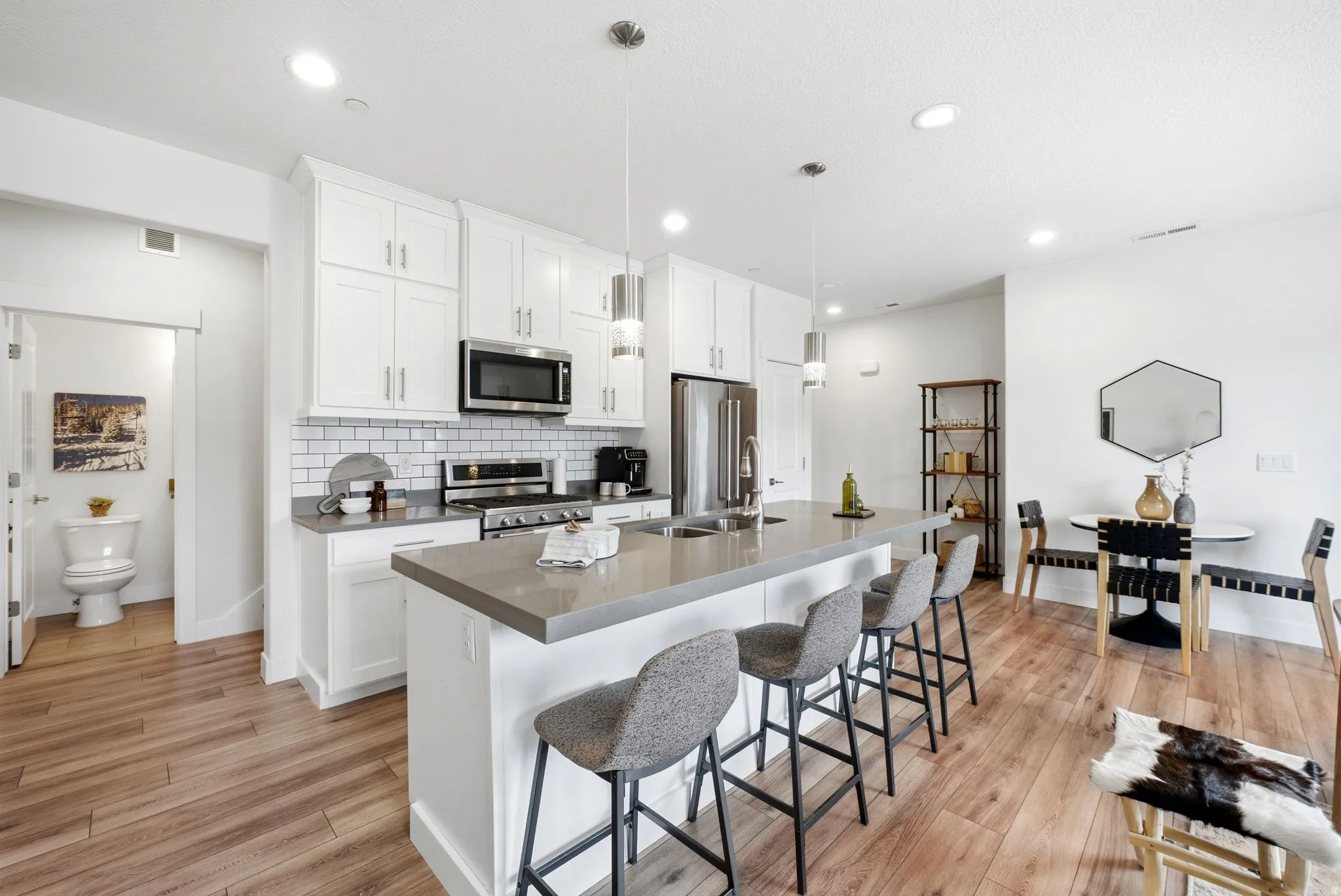 Open-concept kitchen featuring white shaker cabinetry, stainless steel appliances, a subway tile backsplash, and a large island with counter seating