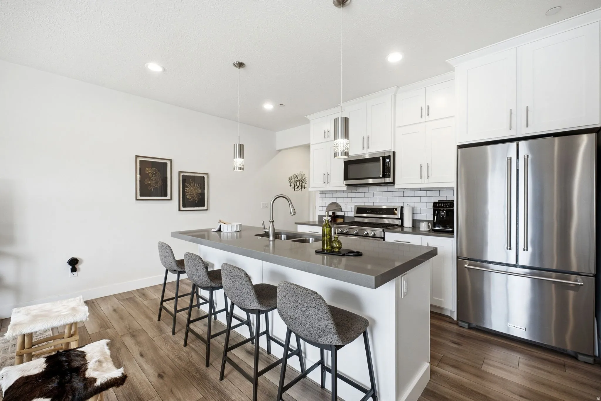 Kitchen featuring a central island with an undermount sink, white cabinetry, stainless steel appliances, wood-finish flooring, and subway tile backsplash