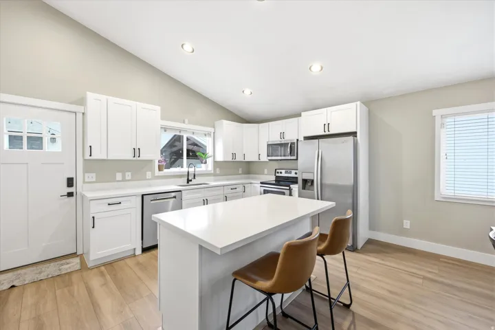 Open-concept kitchen featuring white cabinetry, stainless steel appliances, and a central island with a solid surface countertop