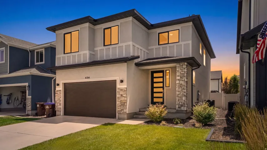 Contemporary two-story residence featuring a stucco exterior with stone accents, a dark garage door, and a modern front entry door with vertical glass inserts