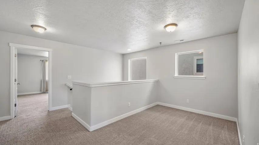 Carpeted upper-level space featuring a contemporary half-wall, two windows, and a neutral color palette throughout