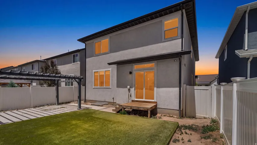Two-story stucco exterior featuring multiple windows, a sliding glass patio door, and a private backyard