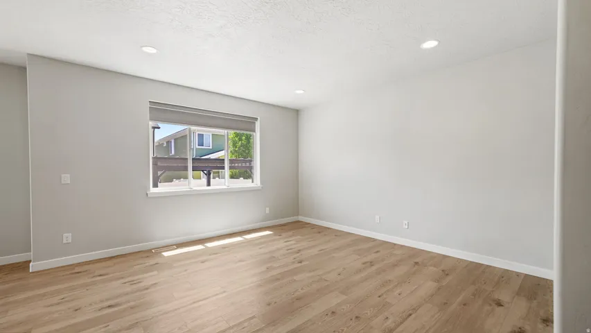 Spacious room with wood-finish flooring, recessed lighting, and a large window with roller shades