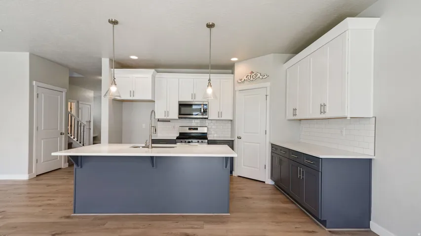 Kitchen featuring a large island with white countertop, pendant lighting, stainless steel appliances, white upper cabinetry, and contrasting lower cabinetry