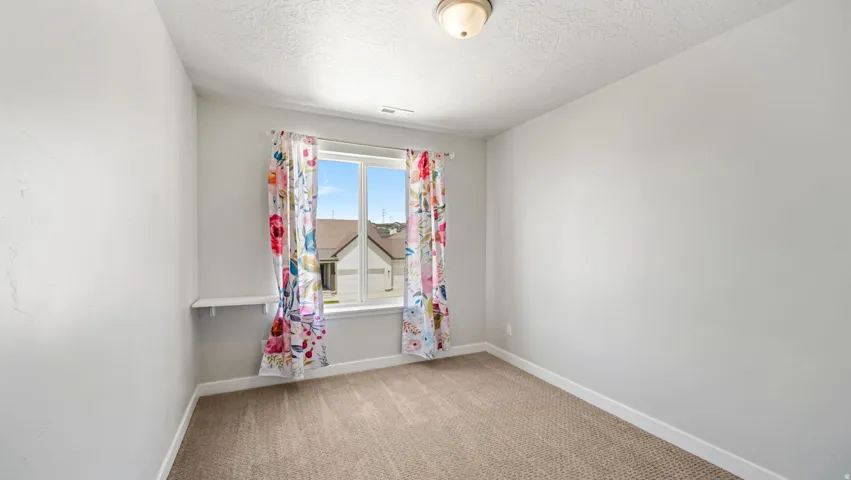 Carpeted room featuring a white-framed window, a built-in wall shelf, and a ceiling-mounted light fixture