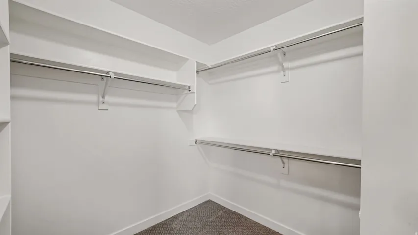 Walk-in closet featuring white shelving, multiple hanging rods, and neutral-toned carpeting