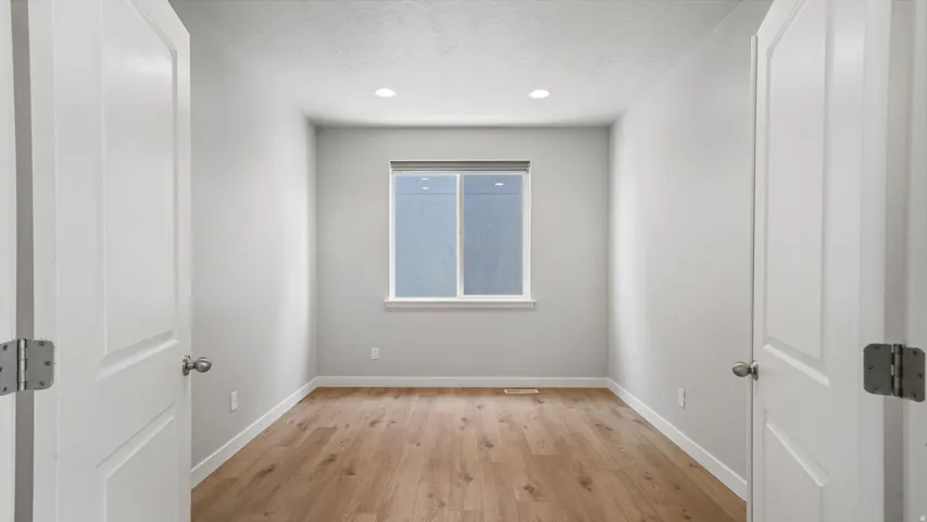 Room featuring wood-finish flooring, recessed lighting, and a single window with a roller shade